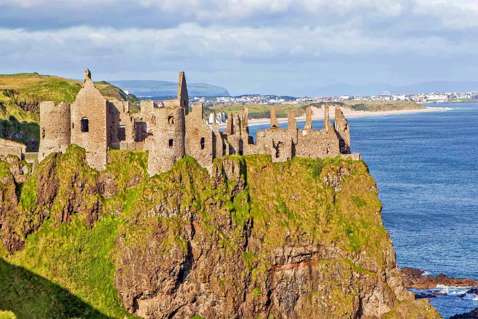 Ireland Visa Dunluce Castle ruins perched on a mossy cliff overlooking the Northern Ireland coastline and beach